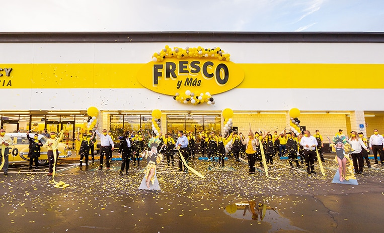 Crowd of people in front of a Fresco Y Mas store front celebrating with balloons and confetti